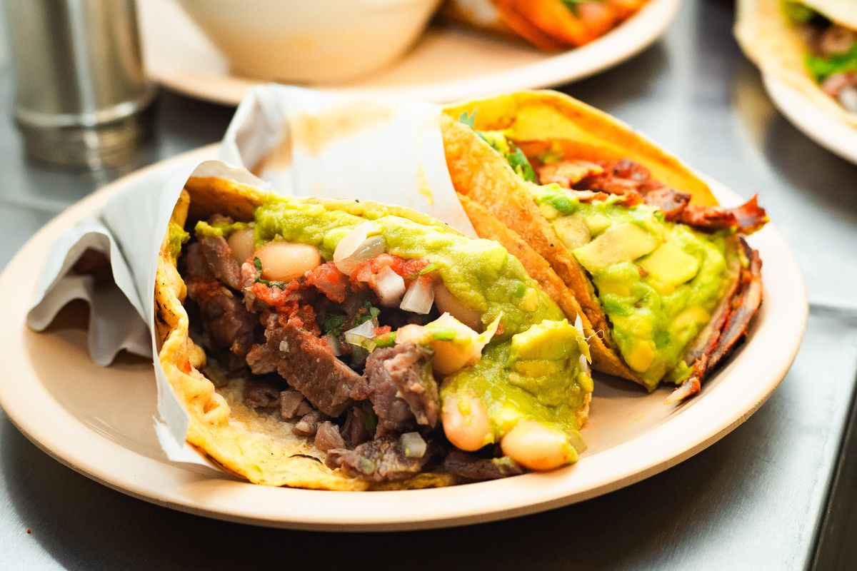 Two tacos overflowing with meat and guacamole.