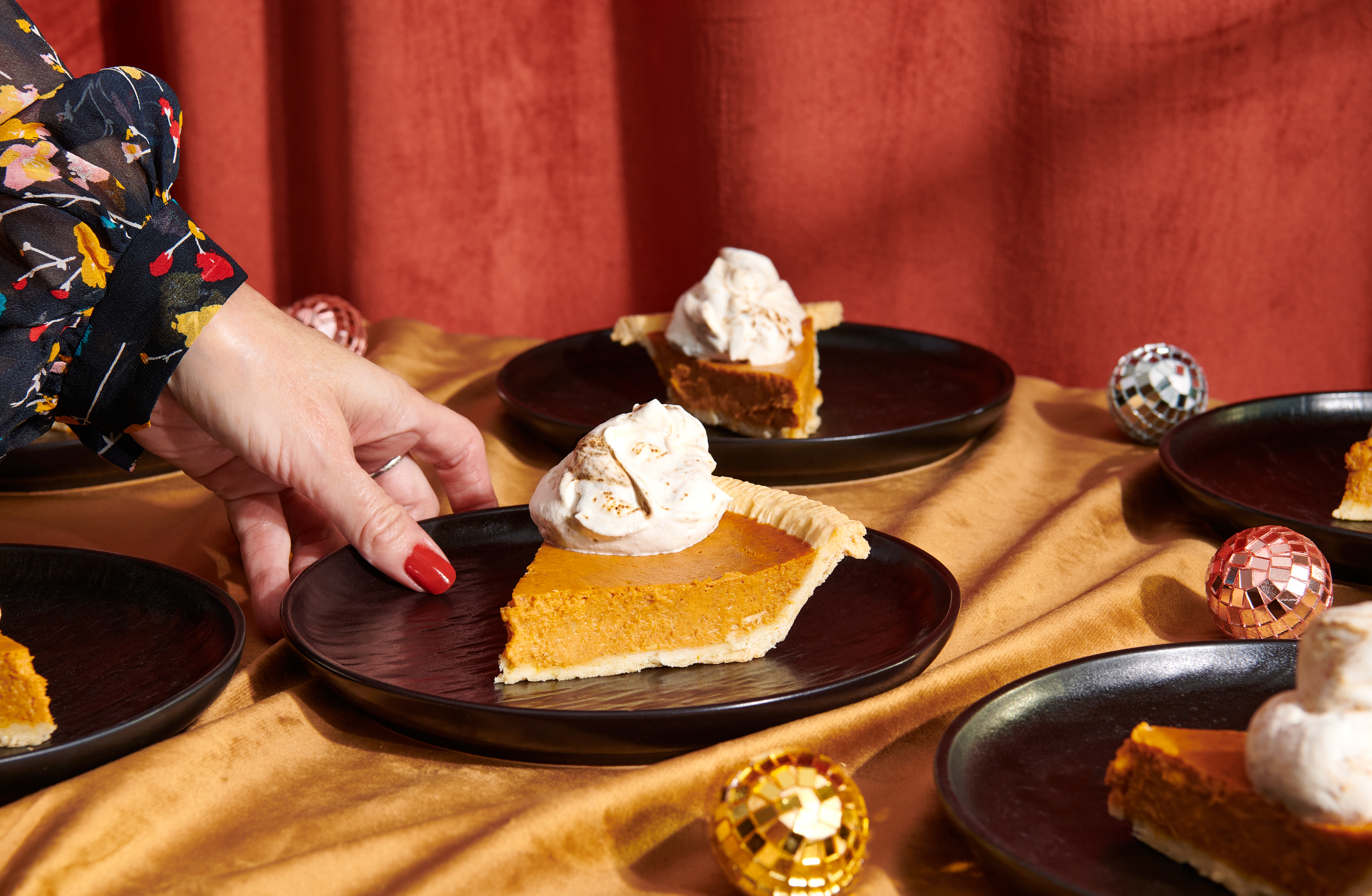 Hand reaching for a plate with a slice of pumpking pie and whipped cream on top.