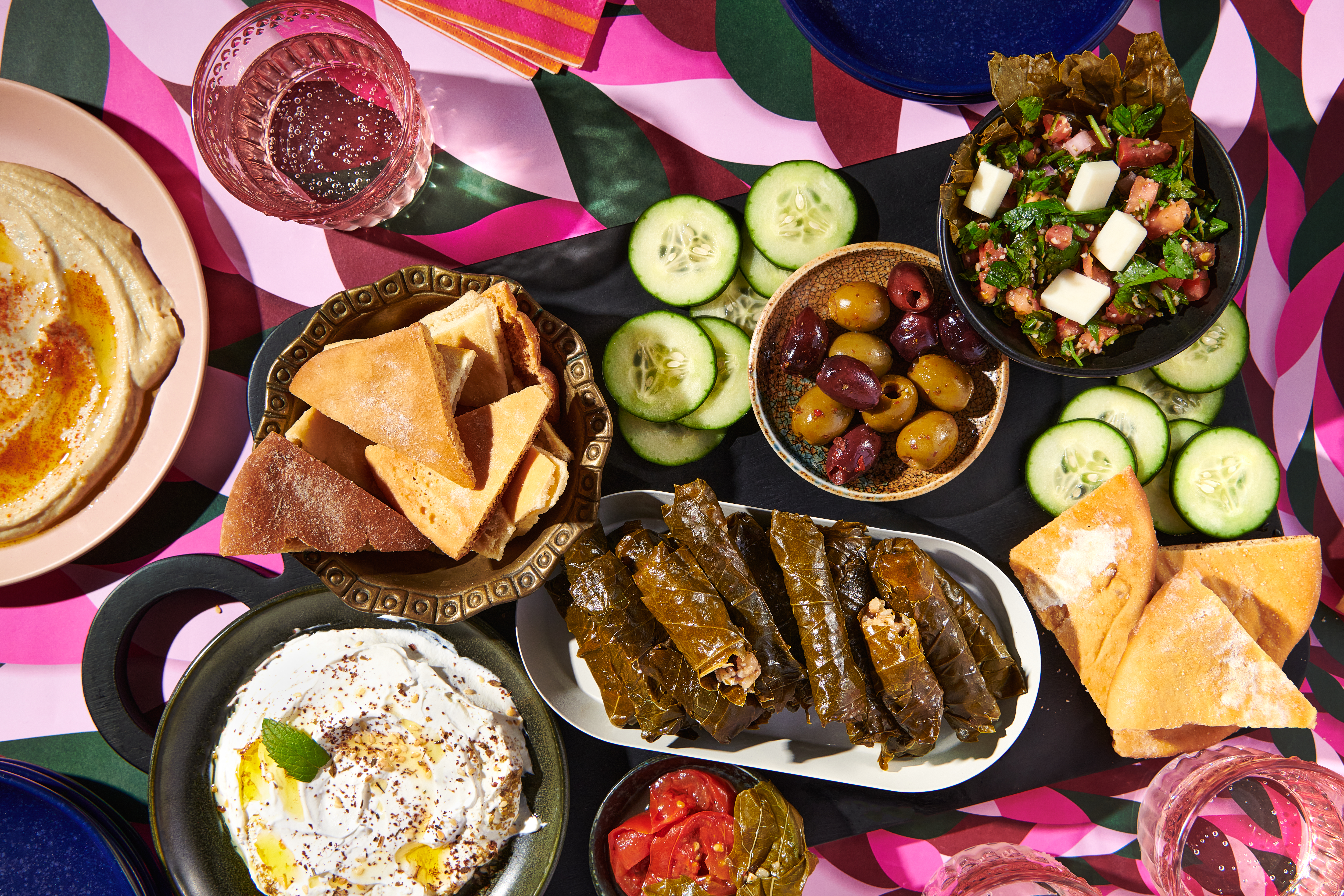 Stuffed grape leaves served on a platter as part of a spread of food including hummus, olives, and pita chips.