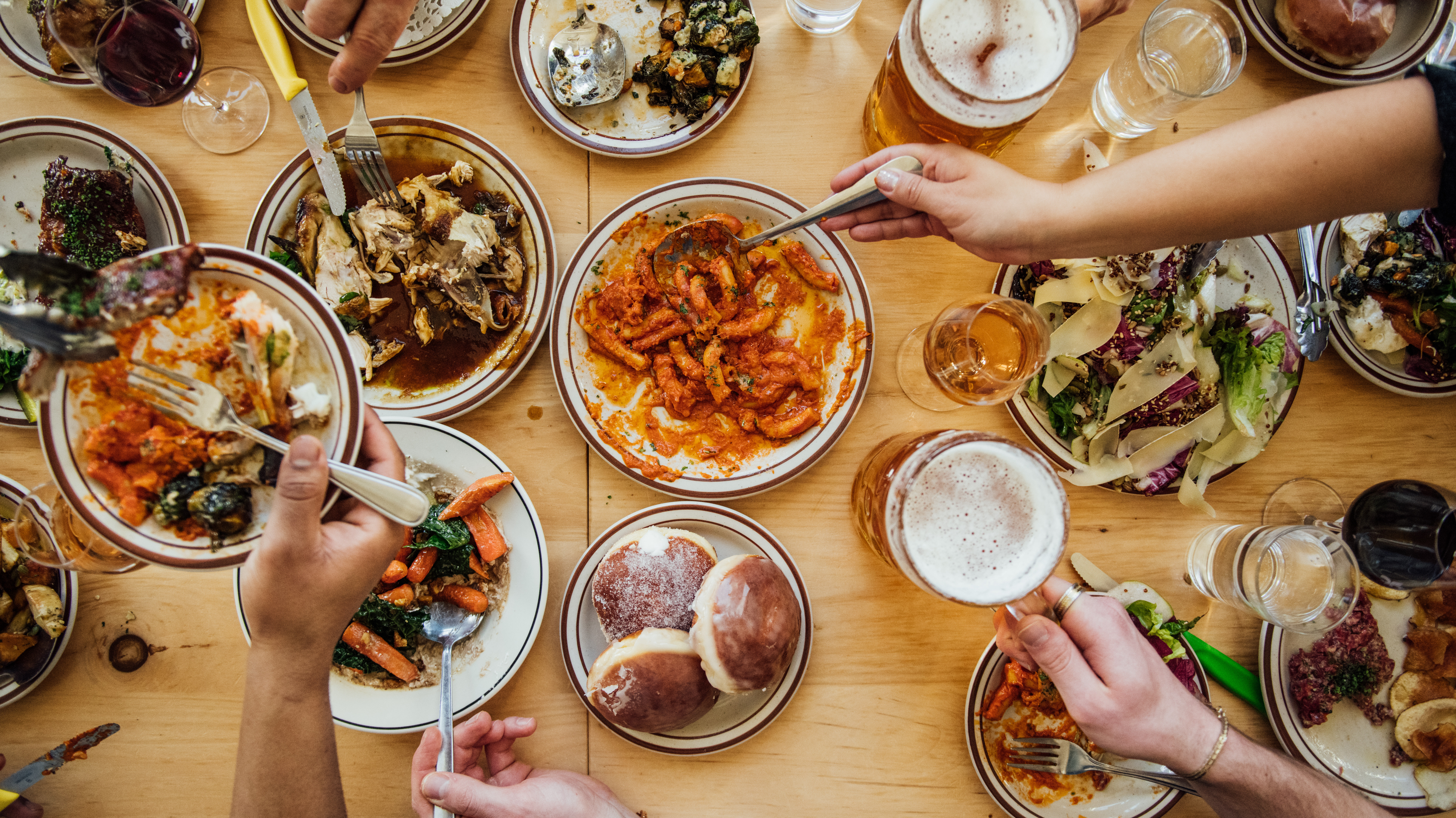 Diners’ hands dig into various dishes on a full table.