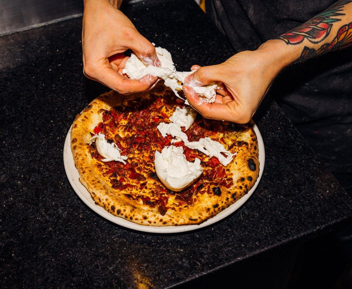 A chef tears cheese to top a pizza.